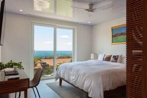 Ein Schlafzimmer mit Bett, Schreibtisch mit Laptop, Stuhl und Blick aufs Meer.
