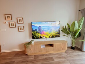 Olohuoneessa on seinälle asennettu taulutelevisio, puinen mediakeskus ja ruukussa oleva huonekasvi.
