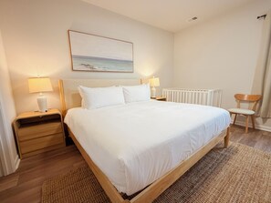Habitación de hotel con una cama grande, dos mesitas de noche con lámparas, un radiador, una silla de madera y un cuadro en la pared.