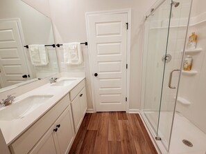 A bathroom with a white vanity, a large mirror, a glass shower enclosure, and a white door. - Spacious 3BR Home with Water Views, Pool Access & Family Amenities (Myrtle Beach)