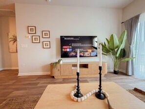 A living room with a flat-screen TV mounted on the wall, a wooden entertainment unit, a large green plant, and a decorative beaded string. - Spacious 3BR Home with Water Views, Pool Access & Family Amenities (Myrtle Beach)