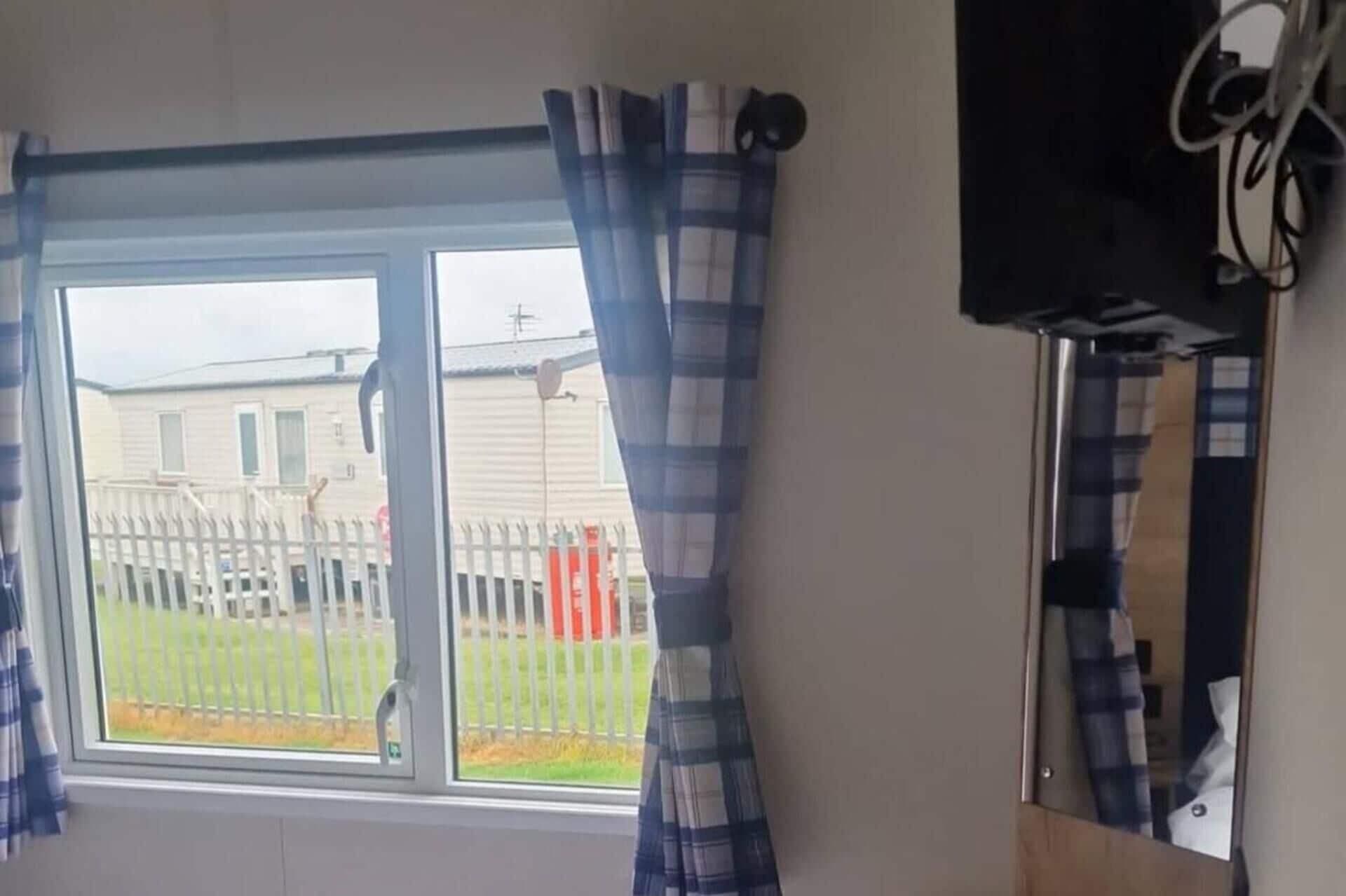 A room with a window, curtains, and a wall-mounted television.