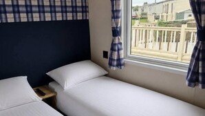 A twin room with two beds, a window with curtains, and a view of a residential area. - 3 Bed - Sleeps 8 - Family & Pet Friendly (Skegness)