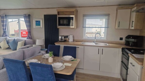 A compact kitchenette with a microwave, toaster, and sink, a dining area with a table set for two, and a living area with a sofa and chairs. - 3 Bed - Sleeps 8 - Family & Pet Friendly (Skegness)