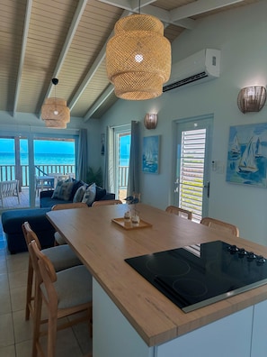A spacious living area with a wooden dining table, a built-in stove, and a view of the ocean through large windows.