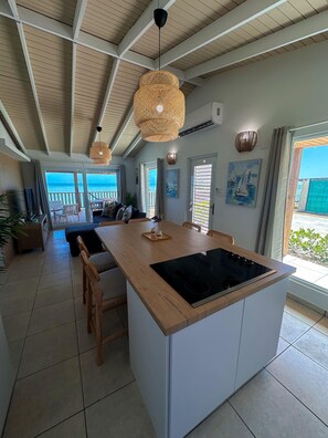 A spacious kitchen with a large island, wooden ceiling, and a view of the sea.