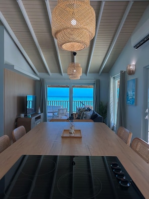 A dining area with a large table, chairs, a television, and a view of the ocean.