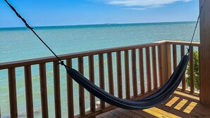 Un pontile in legno con un'amaca, ringhiere di legno e vista sull'oceano.