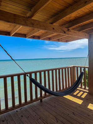 A wooden deck with a hammock, wooden railings, and a view of the ocean.