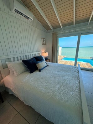 A bedroom with a bed, a nightstand, a lamp, and a view of the ocean.