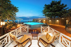 Un espace aménagé au bord de la piscine, avec vue sur l’océan, un barbecue et des sièges d’extérieur.
