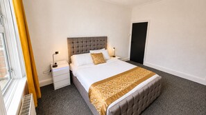 Ein Hotelzimmer mit Bett, Nachttischen, einer Lampe, einem Fenster mit Vorhängen und einer Tür.