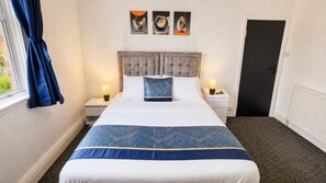 Une chambre d’hôtel avec un lit, deux tables de chevet, une porte et des œuvres d’art accrochées au mur.