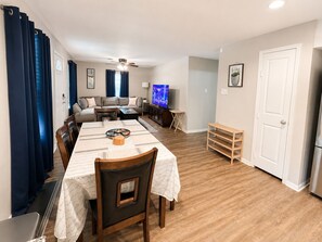 Een woonkamer met een bank, televisie, eettafel en stoelen.