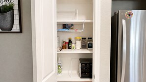 A kitchen with a stainless steel refrigerator, a white pantry with shelves, and a potted plant on the wall. - Private Pool, Near NRG Stadium & Texas Medical & Downtown (Houston)