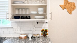 A kitchen with white cabinets, a Texas-themed wall decoration, and a granite countertop with a coffee maker, tea kettle, and a small plant. - Private Pool, Near NRG Stadium & Texas Medical & Downtown (Houston)