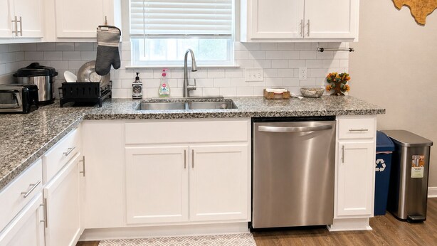 A kitchen with white cabinets, a stainless steel dishwasher, a granite countertop, and a window with blinds. - Private Pool, Near NRG Stadium & Texas Medical & Downtown (Houston)