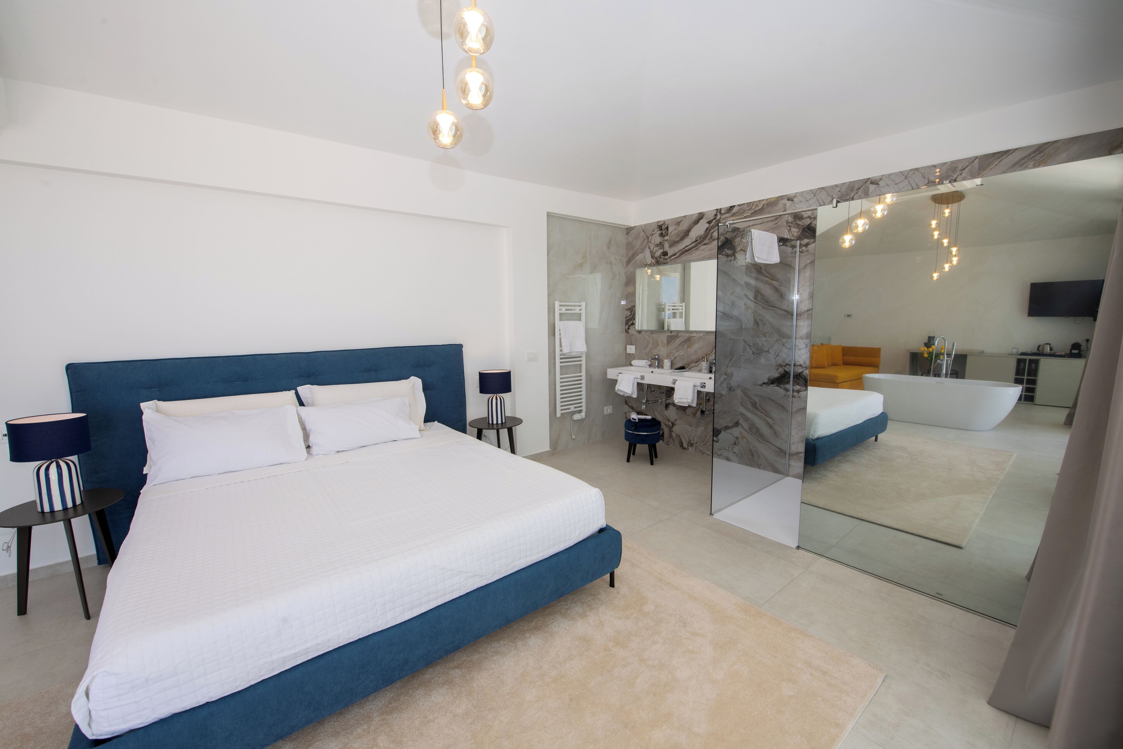 Un dormitorio moderno con una cama grande, mesitas de noche, un espejo y un baño con bañera y lavamanos.