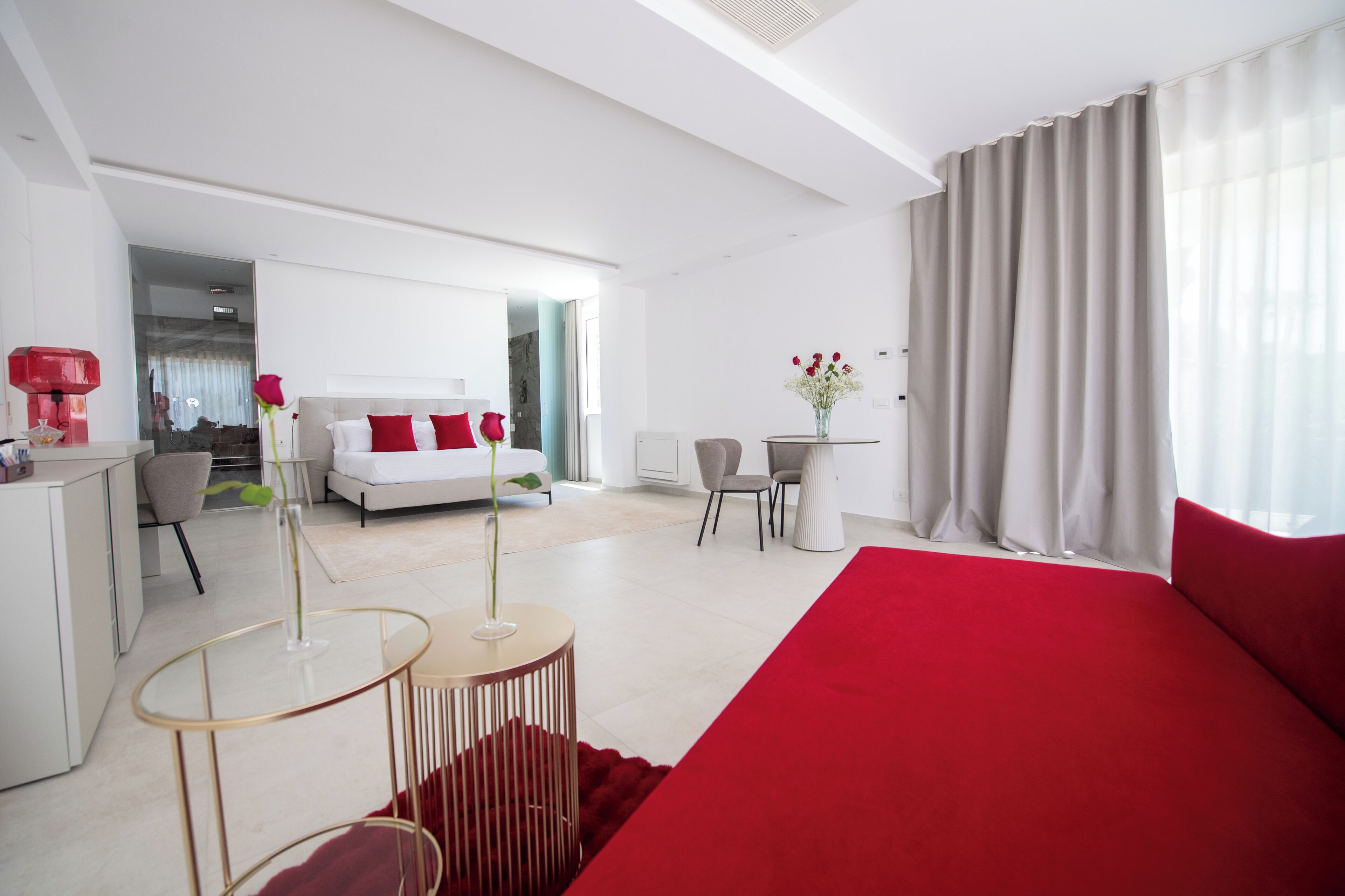 A modern hotel room with a large bed, a desk, a chair, and a small table with a vase of flowers.