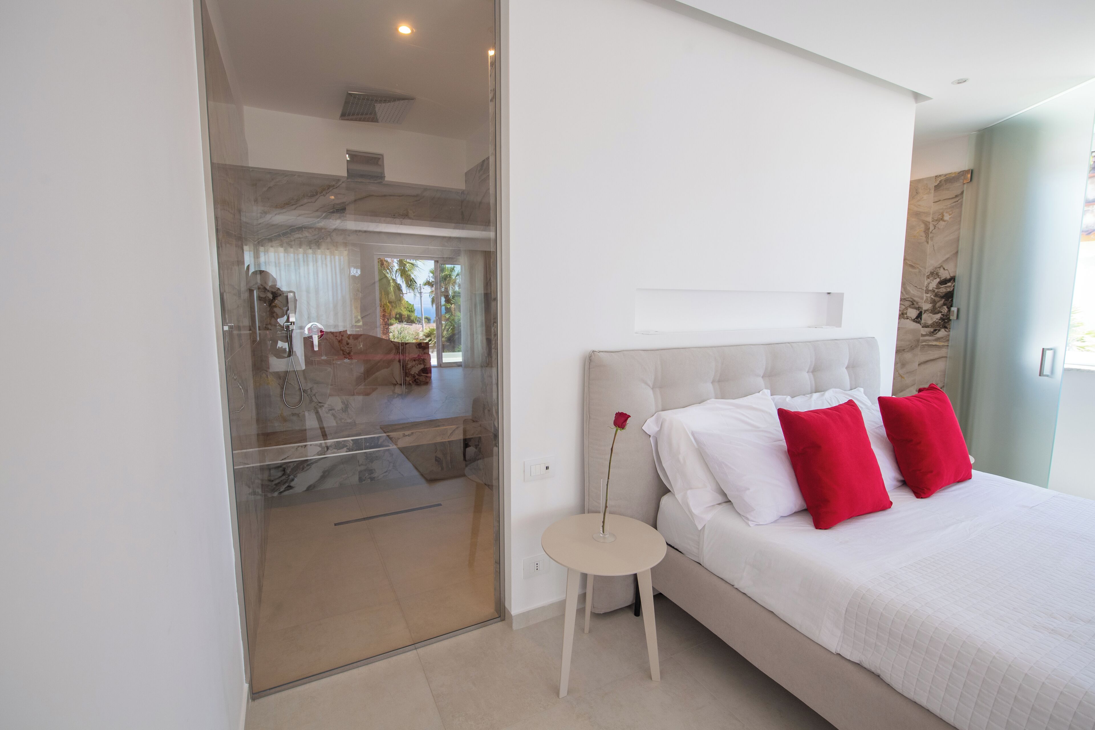 A bedroom with a bed, a small round table, and a glass door leading to a balcony.