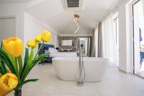 A modern bathroom with a freestanding bathtub, a shower, and a toilet. There is a potted plant with yellow flowers in the foreground.