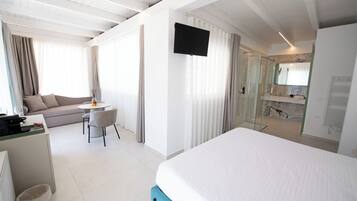 Een hotelkamer met een bed, een bureau met stoel, een bank, een aan de muur bevestigde televisie en een douche.