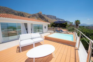 Une terrasse avec une piscine, des meubles blancs et une vue sur les montagnes.