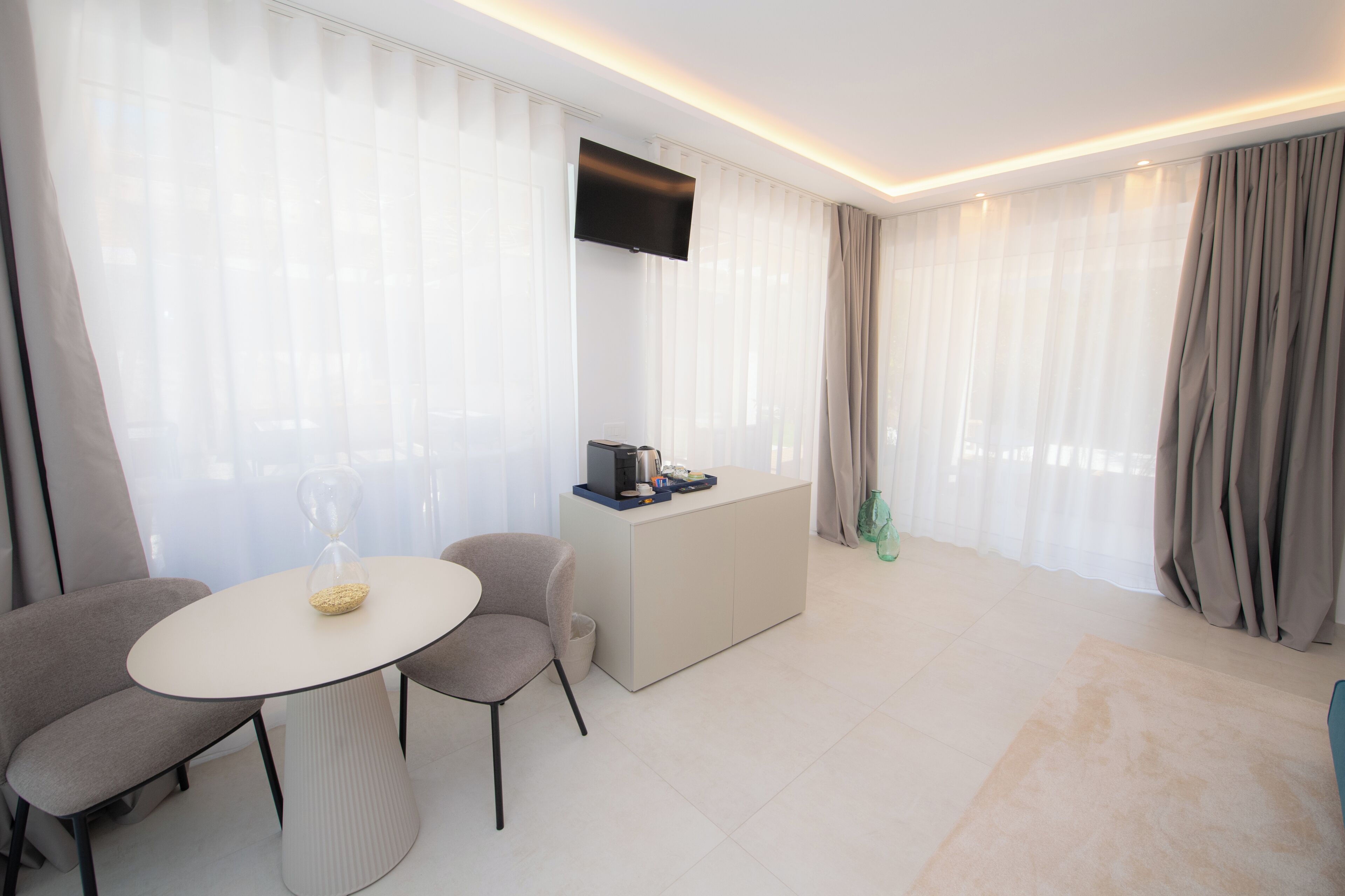 A modern living room with a round table, two chairs, a coffee station, and a TV mounted on the wall.