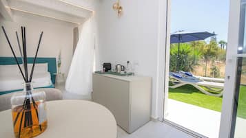 Een moderne slaapkamer met een bed, nachtkastje, klein kastje en uitzicht op een terras met tafel en stoelen.