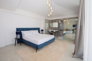 A modern bedroom with a large bed, bedside tables, a bathroom with a shower, and a TV mounted on the wall. - Novaeos (Terrasini)