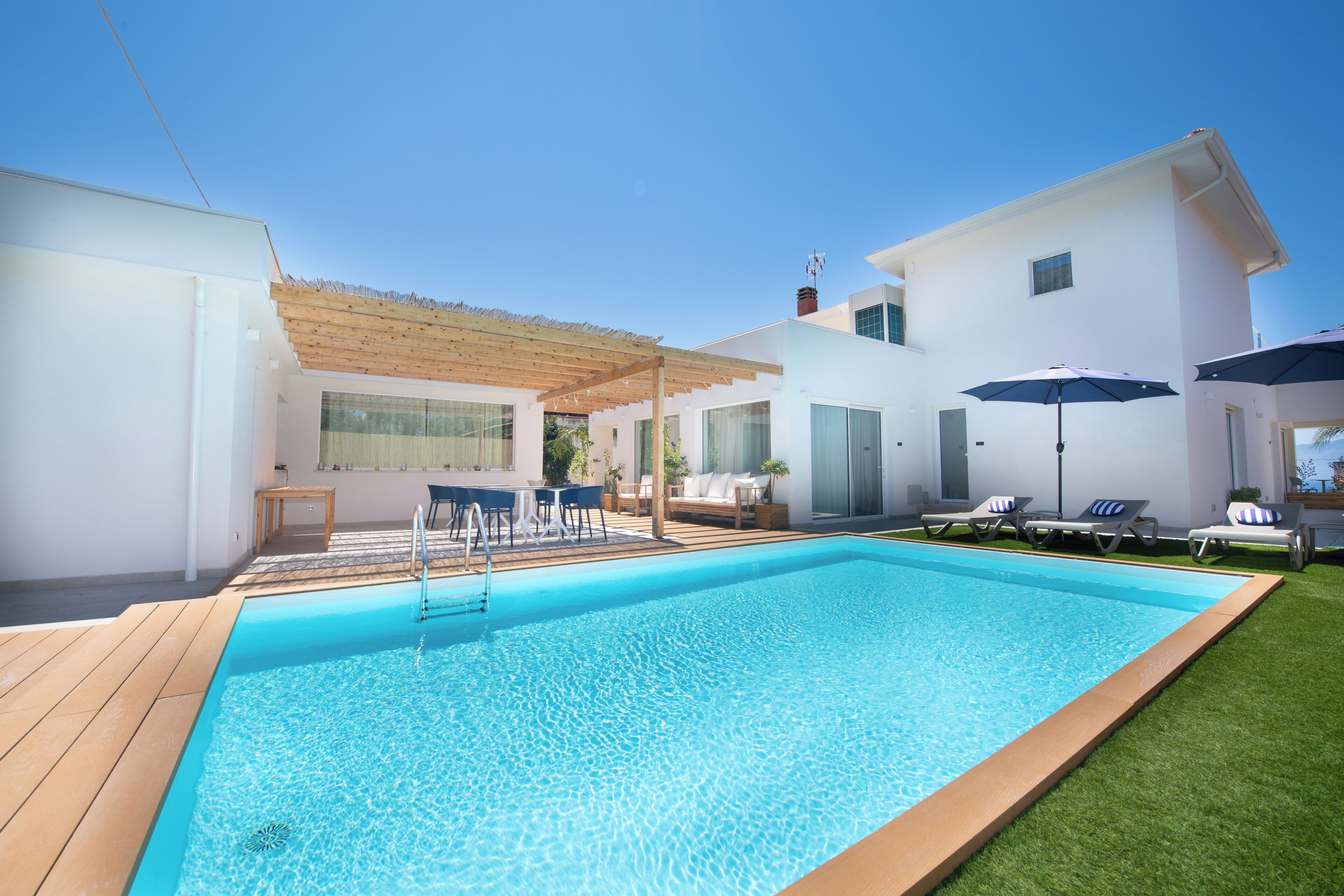 A modern outdoor swimming pool with a wooden deck, lounge chairs, and a pergola.
