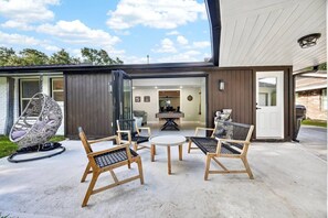 Ein modernes Haus mit einer Terrassenfläche, ausgestattet mit Korbstühlen, einem runden Tisch und einer Hängematte.