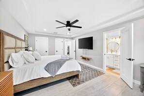 Ein Schlafzimmer mit Bett, Deckenventilator, Fernseher, Spiegel und Tür.