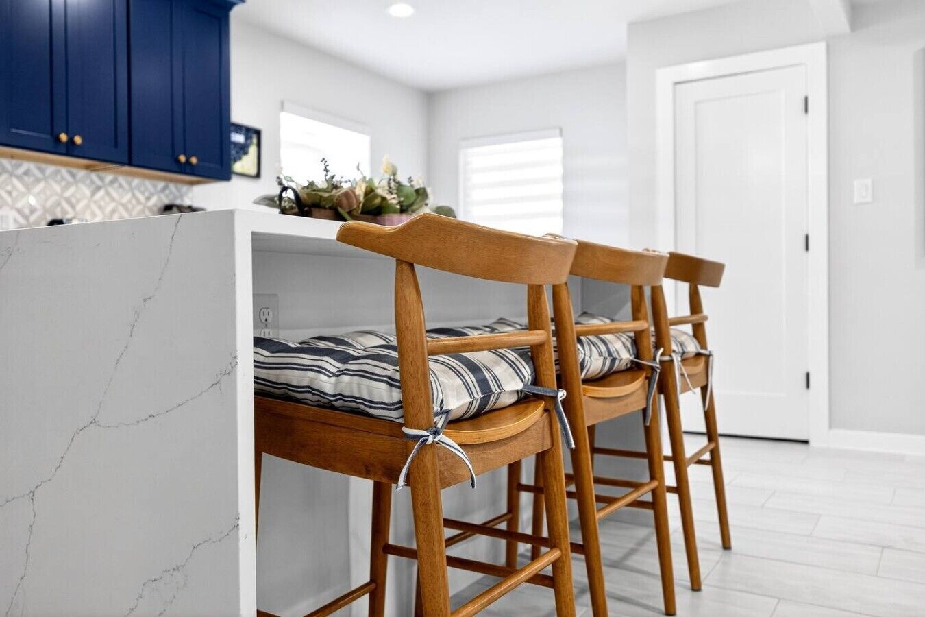 Een moderne keuken met houten barstoelen, een marmeren aanrechtblad en uitzicht op de aangrenzende woonkamer.