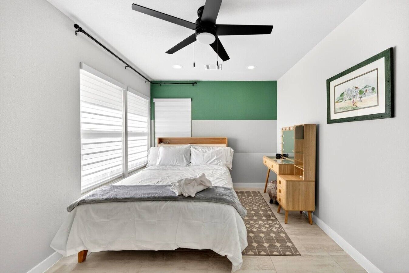 A bedroom with a bed, a ceiling fan, a dresser with a mirror, and a framed picture on the wall.