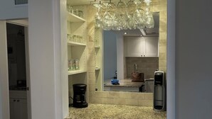 Cozinha com bancada de granito, armários brancos, cafeteira, filtro de água e luminária pendente.