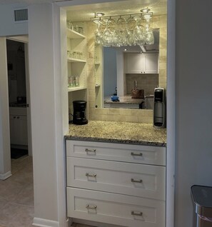 A kitchen with a granite countertop, white cabinets, a coffee maker, a water dispenser, and a hanging light fixture. - Beautiful 2-bedroom, 2-bathroom condo in charming St. Augustine Beach. (St. Augustine)