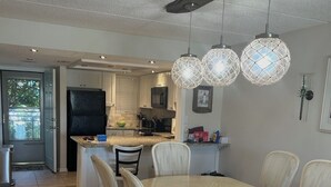 Uma cozinha moderna com área de refeições, destacando uma mesa grande e cadeiras, luminárias pendentes e uma geladeira visível.
