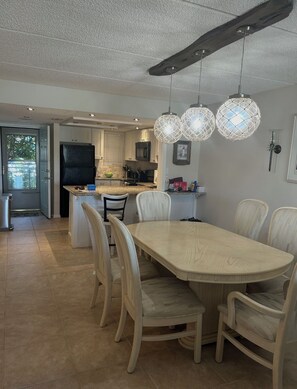 A modern kitchen with a dining area, featuring a large table and chairs, pendant lights, and a visible refrigerator. - Beautiful 2-bedroom, 2-bathroom condo in charming St. Augustine Beach. (St. Augustine)