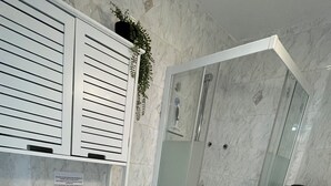 Un baño con inodoro, ducha con mampara de vidrio y lavamanos.