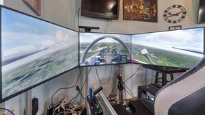 A cockpit simulator with multiple monitors, a steering wheel, and a control panel. - Cozy retreat w/ pool & backyard (Clermont)
