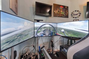 A cockpit simulator with multiple monitors, a steering wheel, and a control panel. - Cozy retreat w/ pool & backyard (Clermont)