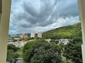 Eine Stadtsicht mit Wohngebäuden, einem Hügel mit Grünflächen und einem bewölkten Himmel.