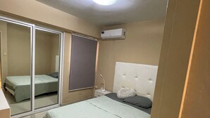 Un dormitorio con cama, mesita de noche, espejo, puerta corrediza y equipo de aire acondicionado.