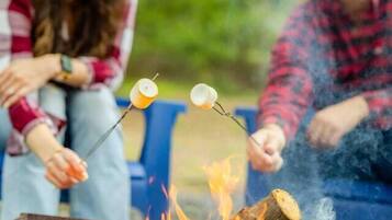 Two people roasting marshmallows over a campfire in an outdoor setting.