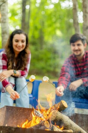 Two people roasting marshmallows over a campfire in an outdoor setting.