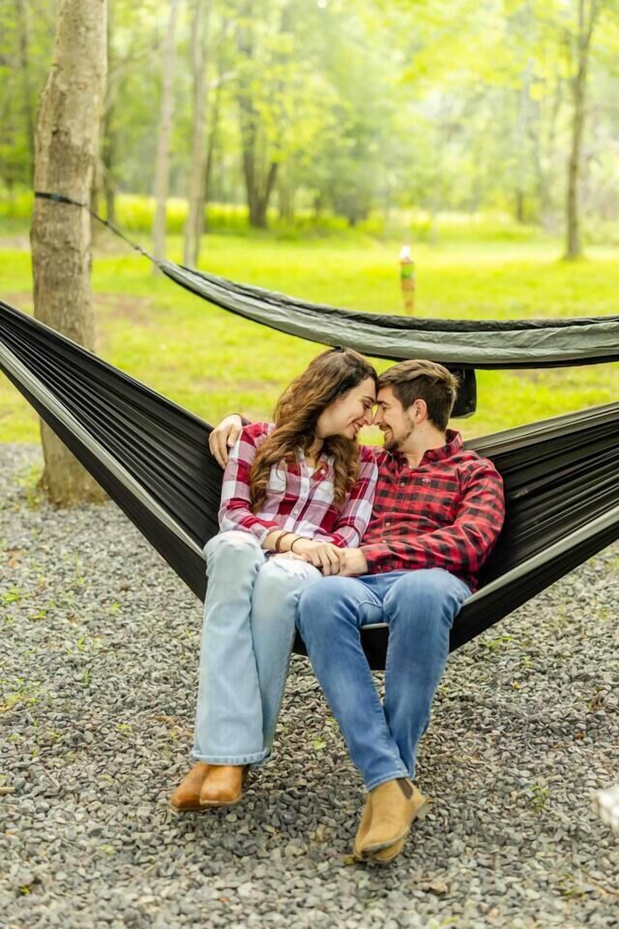 A hammock in a park with trees and gravel ground.