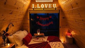 A cozy, triangular wooden cabin room with a bed, a small table, and a wall sign that reads 'I LOVE U.'