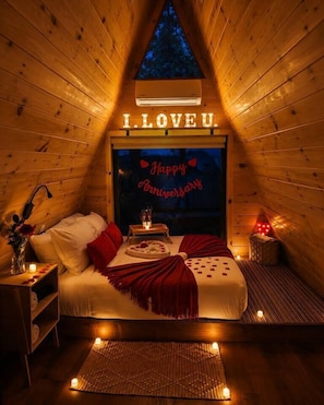 A cozy, triangular wooden cabin room with a bed, a small table, and a wall sign that reads 'I LOVE U.'