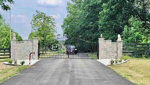 A gated entrance with a metal gate, stone pillars, and a paved driveway leading to a vehicle.